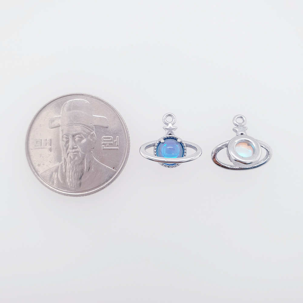 써지컬 우주 행성 펜던트입니다. 100원짜리 동전과 비교하였습니다. 100원짜리 동전은 왼쪽에 있고, 그옆에는 오른쪽에는 우주행성펜던트의 앞면과 뒷면을 놓고 동전과 비교하였습니다.