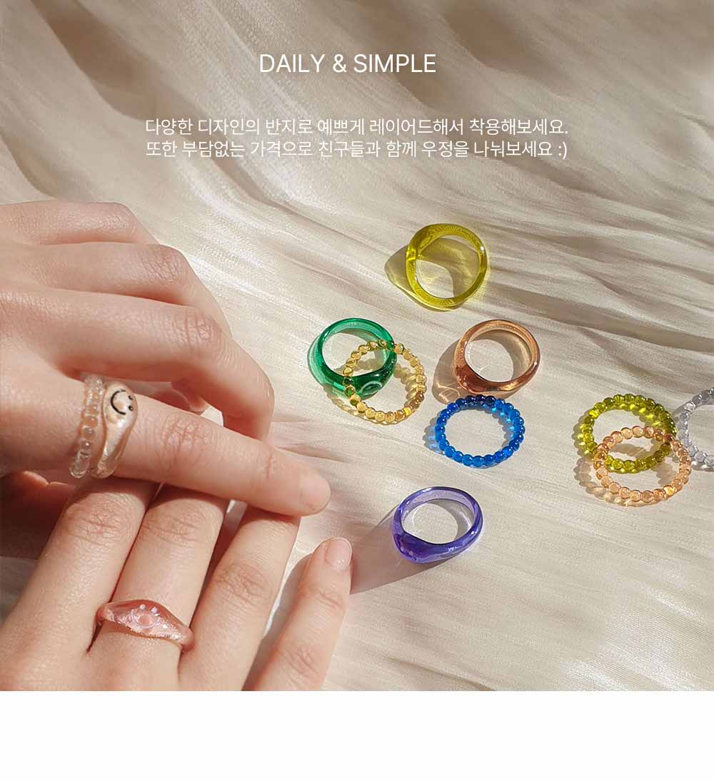 이 이미지는 실크천을 배경으로 오른쪽에는 다양한 반지들이 자유롭게 놓아져있고, 왼쪽에는 다양한 반지를 착용한 양쪽손이 보입니다. 왼손 검지에 얇은 반지와 스마일반지를 레이어드하고 오른손엔 핑크 스마일 반지를 착용하여 손을 포개고 있다. 이 이미지는 "다양한 디자인의 반지로 예쁘게 레이어드해서 착용해보세요. 또한 부담없는 가격으로 친구들과 함께 우정을 나눠보세요"라는 문구를 담고있다.