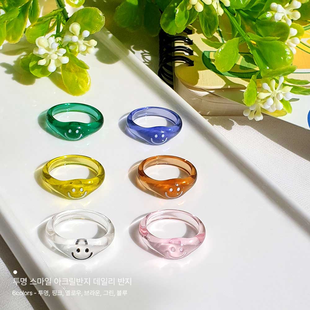 이 이미지는 세로로 길고 평평한 접시에 6컬러의 투명 스마일 아크릴 반지가 세로2열로 나란히 놓여져있습니다. 그리고 위에는 작은 잎파리가 있는 꽃이 있습니다.
투명 스마일 아크릴 반지의 특징은 앞부분에 귀여운 스마일 모양이 매력적입니다. 모양도 라운딩되어있고 무게감도 가벼워서 부담스럽지 않게 착용할 수 있는 반지입니다.
